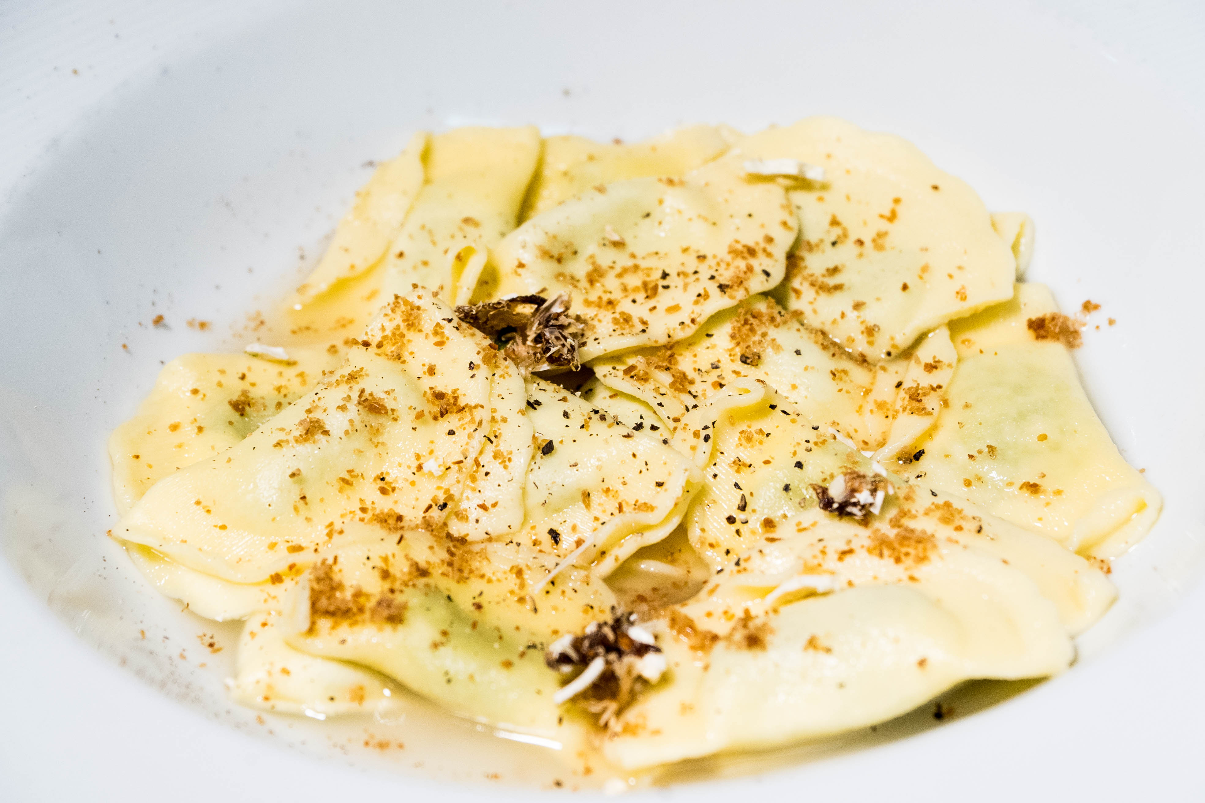 A white bowl of ravioli with spices on it.